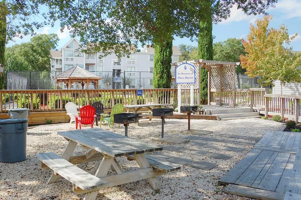 A cheerful community grilling and picnic area featuring multiple picnic tables, grill stations, a gazebo, and an array of colorful chairs. The space feels welcoming and ideal for social gatherings or alfresco dining.