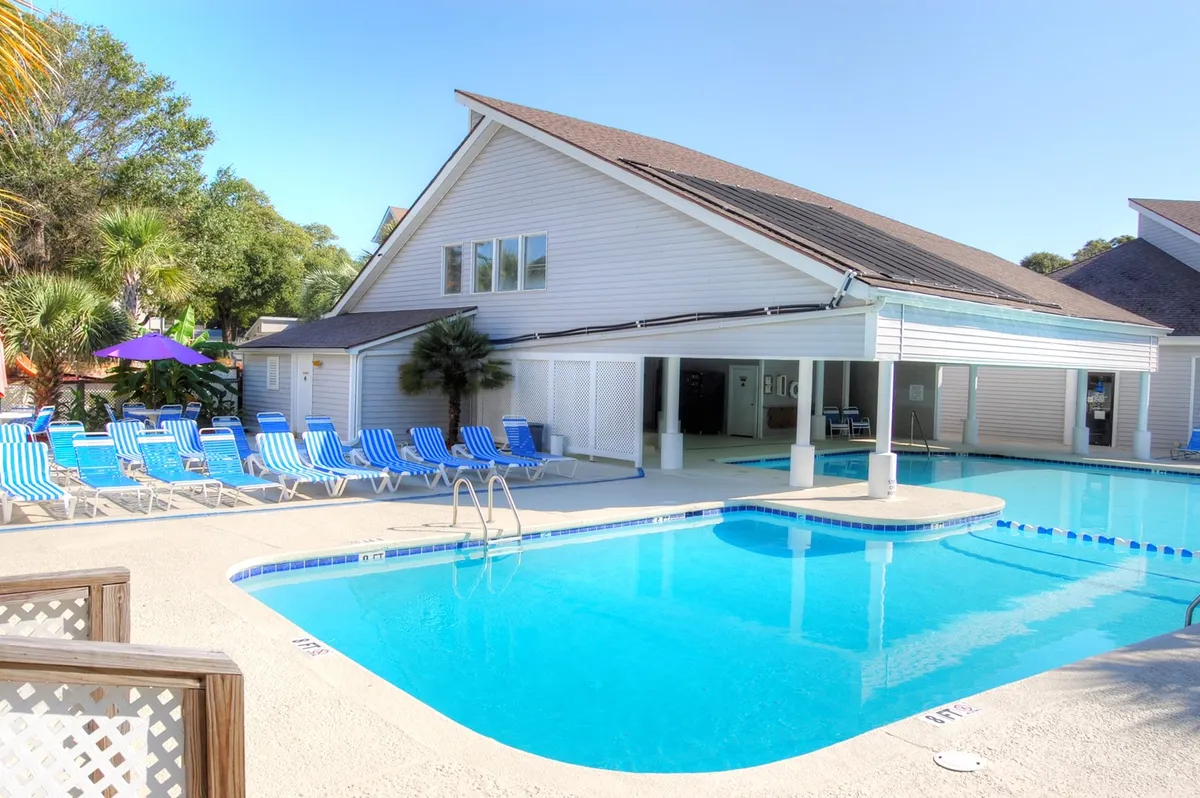 The image showcases the inviting outdoor amenities of the condo: a sparkling swimming pool surrounded by comfortable lounge chairs and a welcoming clubhouse. The scene is bathed in natural light, suggesting a relaxed, resort-style atmosphere ideal for leisurely swims, sunbathing, and gathering with friends or family. The pool area is spacious, with room for both quiet relaxation and community activities, hinting at opportunities for sunset swims and poolside socializing.