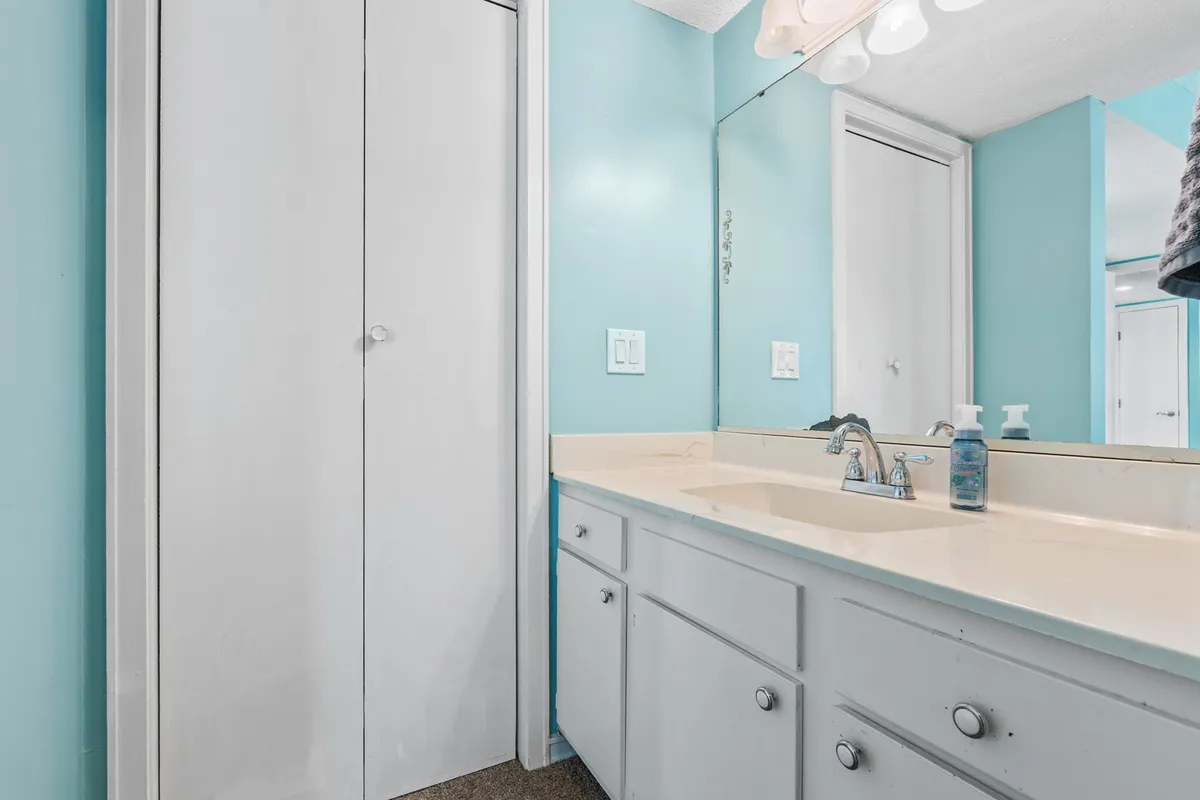 A serene bathroom scene featuring light blue walls, white cabinetry, and a vanity mirror. The space feels fresh, clean, and inviting, highlighting opportunities for self-care and relaxation.