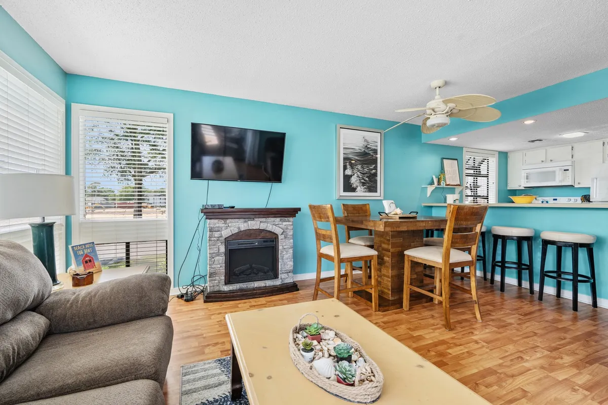 A welcoming living area featuring a comfortable sofa, dining table, TV, and a decorative fireplace, all set against colorful wall art. The room radiates warmth and offers an inviting space for relaxing or entertaining guests.