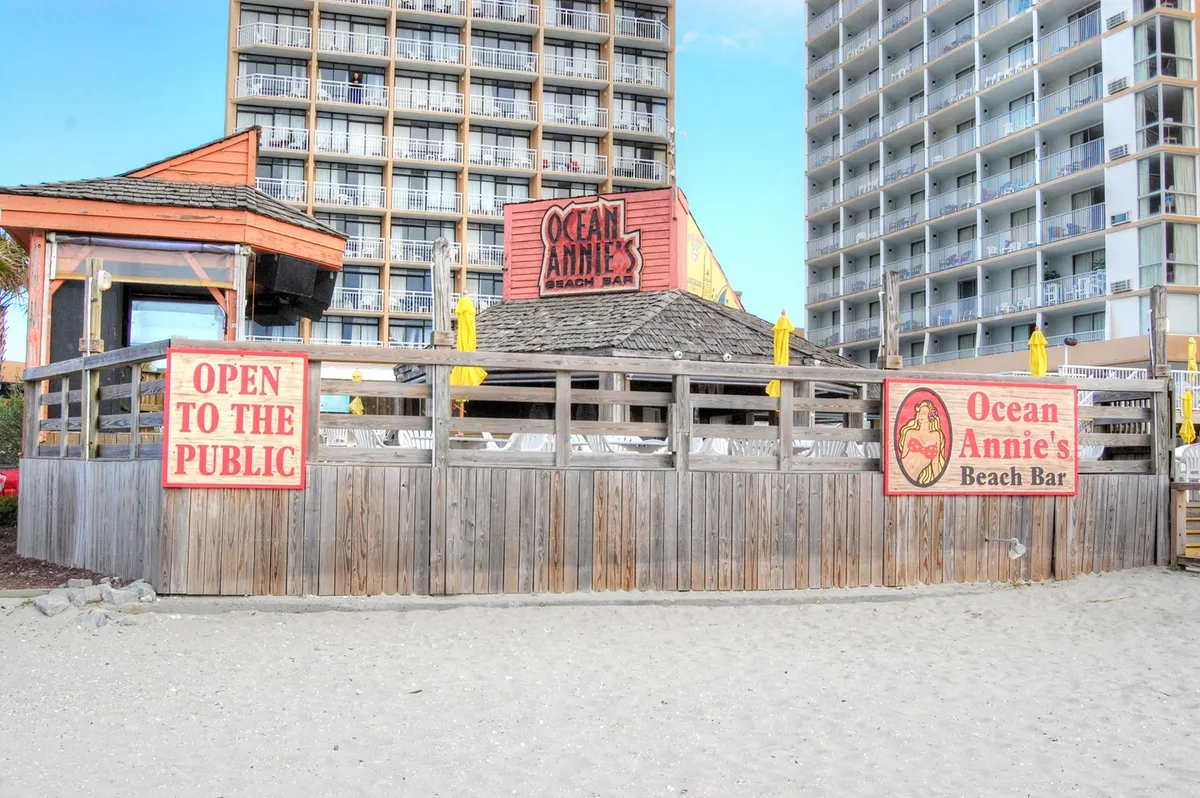 This image features the recognizable Ocean Annie's Beach Bar sign and beach area, with a relaxed beachfront atmosphere, wooden fencing, and clear sightlines to sandy surroundings.