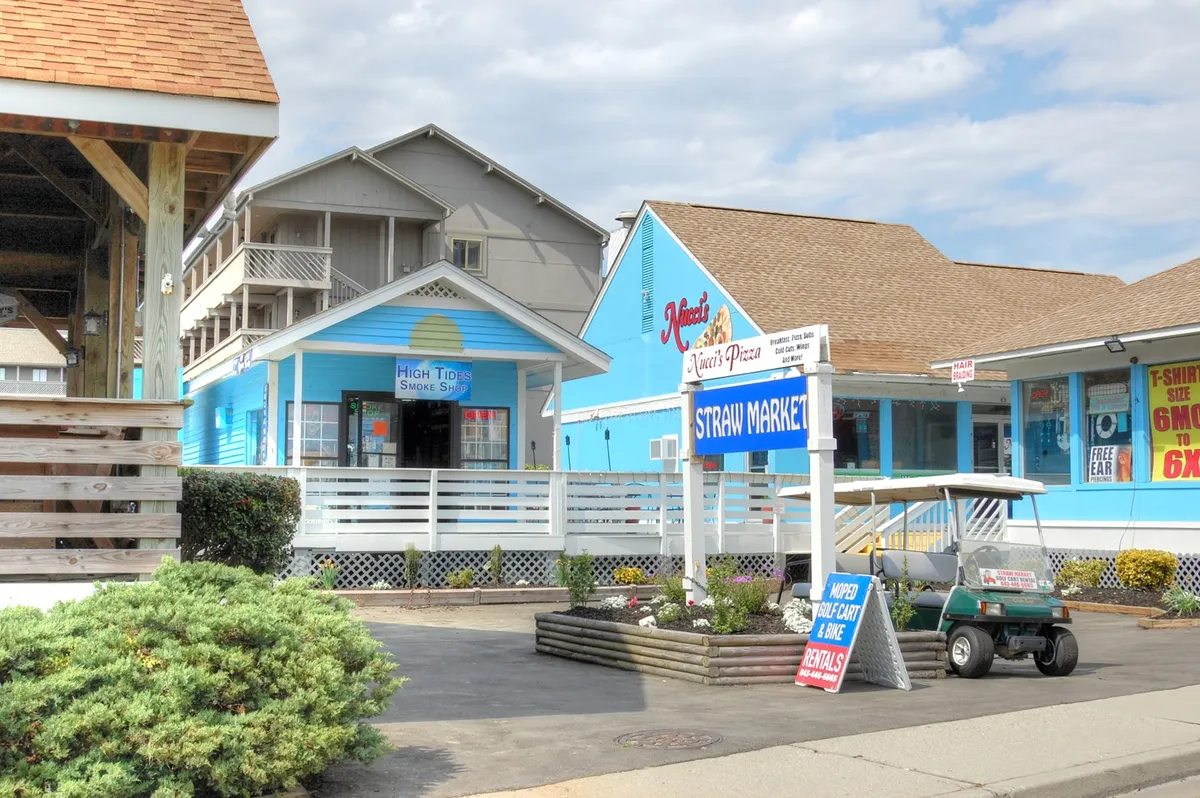 A colorful streetscape with blue buildings, a market sign, and a golf cart parked nearby. The scene radiates a cheerful, inviting atmosphere, suggesting opportunities for shopping, casual dining, and exploring local boutiques with a loved one.